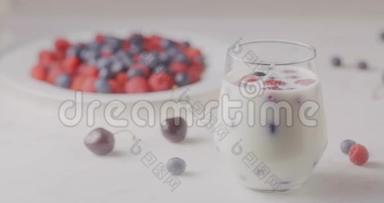 从一个有浆果和牛奶的玻璃杯中调焦，放在一个有成熟蓝莓和樱桃的盘子里